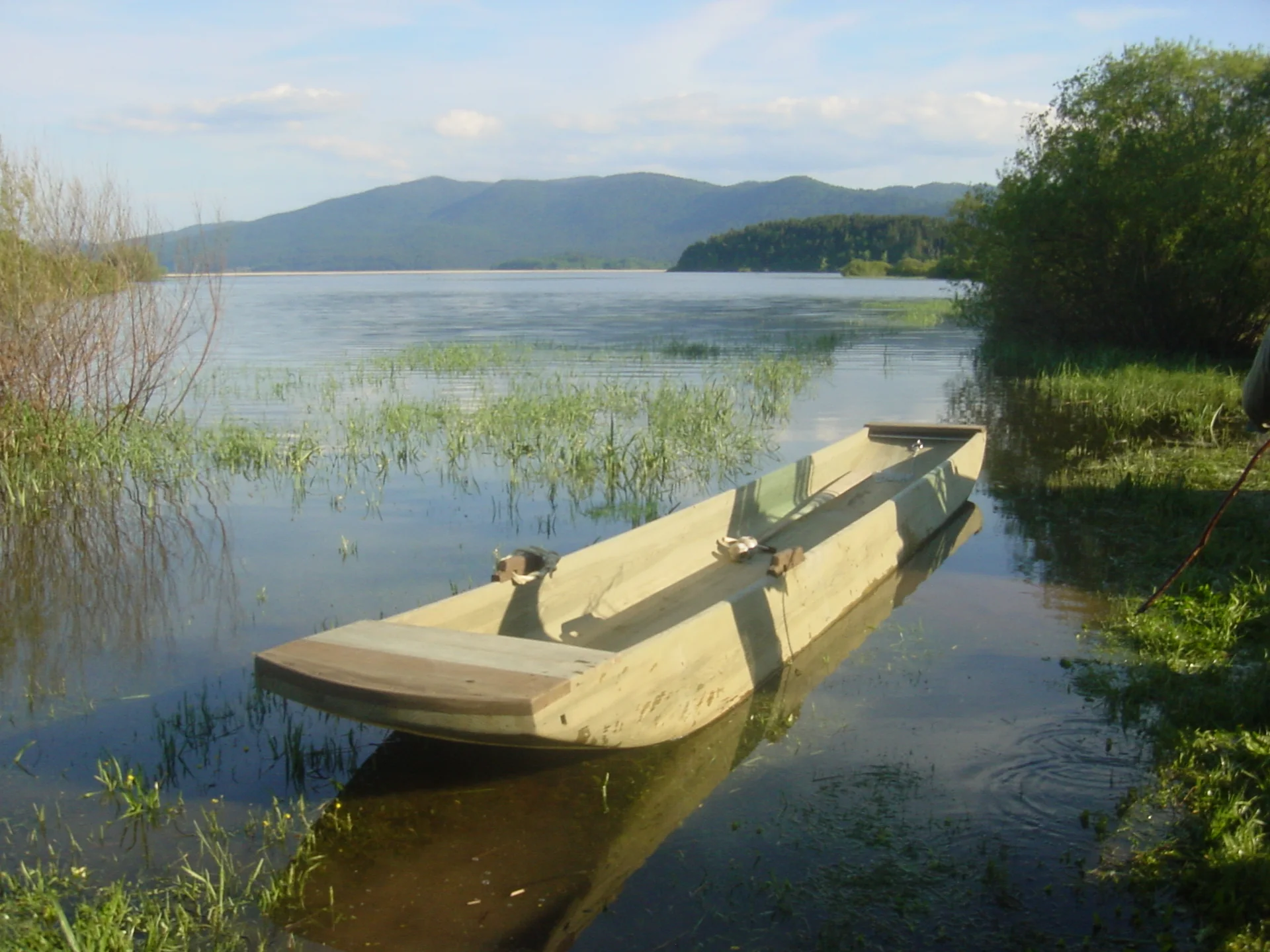 Poplavljeno Cerkniško jezero z drevakom in gorami v ozadju